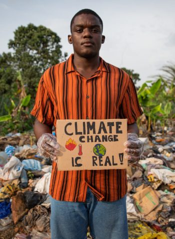 African boy holds a sign in his hand with the words: "climate change is real" and protests in front of an illegal landfill